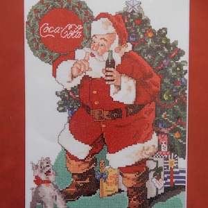 May include: Cross-stitch image of Santa Claus holding a Coca-Cola bottle, with a Christmas tree and gifts in the background. A small dog with a red collar stands in front of Santa. The Coca-Cola logo is in a wreath.