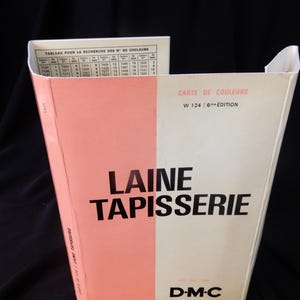 May include: A vintage DMC Laine Tapisserie color chart box. The box is divided into pink and cream sections with the text "LAINE TAPISSERIE" in large black letters. The box also includes a color reference chart and the text "CARTE DE COULEURS".
