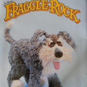 May include: A Butterick Craft sewing pattern envelope for a Jim Henson's Fraggle Rock Sprocket dog plush toy. The cover features a photograph of a dark gray, shaggy-textured dog with white paws, a white muzzle, and a pink tongue sticking out.