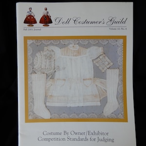 May include: A magazine cover for the Doll Costumer's Guild, Fall 2001 Journal, Volume 10, No. 4. The cover features a white doll dress, socks, and bonnet. The text reads "Costume By Owner/Exhibitor Competition Standards for Judging."