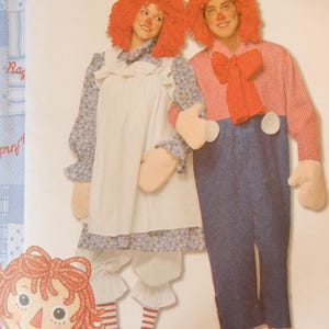 May include: Two people dressed in Raggedy Ann and Andy costumes. The Raggedy Ann costume includes a white apron, blue floral print sleeves, and red striped socks. The Andy costume features a red and white checkered shirt, blue overalls, and a red bow tie.