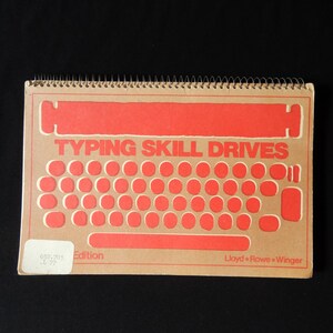 May include: A brown spiral bound book with the title "Typing Skill Drives" in red letters. The cover features a red outline of a typewriter keyboard. The book has a label on the bottom left corner that says "650-203 Edition". The bottom right corner says "Lloyd + Rowe + Winger".