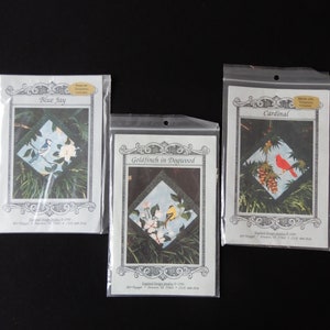 May include: Three iron-on applique patterns for quilting. The patterns feature a blue jay, a goldfinch in dogwood, and a cardinal. Each pattern includes a small image of the finished design and instructions for use.