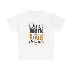 May include: White t-shirt with the text "Quiet Work Loud Results" in navy blue and gold lettering. The design is centered on the shirt, with a cream-colored background. The shirt is made of a soft, comfortable material.