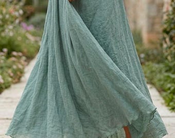 May include: A floor-length sage green skirt with a gathered elastic waistband and a textured, flowing fabric. The skirt features a loose, A-line silhouette that reaches the ankles, paired with simple brown leather sandals with thin straps.