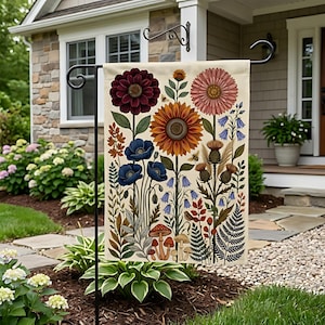 Könnte beinhalten: Eine rechteckige Gartenflagge mit einer botanischen Illustration auf cremefarbenem Hintergrund. Das Design zeigt eine zentrale Sonnenblume, eine dunkelrote Dahlie, ein rosa Gänseblümchen, blaue Mohnblumen, Glockenblumen, Disteln, Farne und kleine Pilze.