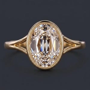 May include: A gold ring featuring a large, oval-cut, champagne-coloured centre stone set within a milgrain-detailed bezel. The band is crafted from polished yellow gold and features a split-shank design that tapers towards the central setting.