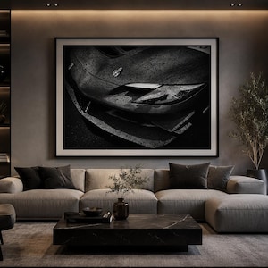 May include: A large rectangular wall art print featuring a black and white close-up of a sports car front end with visible raindrops on the hood, framed in a thin black border and displayed above a beige sectional sofa in a living room.
