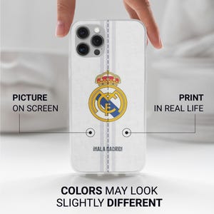 Op de afbeelding: Een doorzichtig smartphonehoesje met het logo van voetbalclub Real Madrid in geel, blauw en rood, gecentreerd op een witte achtergrond met verticale lichtgrijze strepen en de tekst &iexcl;HALA MADRID! in het zwart nabij de onderrand.