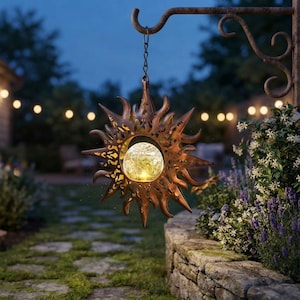 May include: A hanging sun-shaped metal lantern with a bronze finish and intricate cut-out details. The center features a spherical, crackled glass globe that emits a warm, glowing light, suspended from a curved metal hook by a thin chain.
