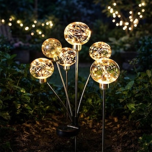 May include: A solar-powered garden light fixture featuring five clear glass globes on thin metal stems. Each globe contains warm white fairy lights that emit a soft glow. The structure is supported by a central base stake for ground placement.