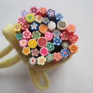 Puede incluir: Una colección de diseños de flores y espirales de arcilla polimérica de colores en una bolsa de tela amarilla. Los diseños son perfectos para el arte de uñas y la artesanía.