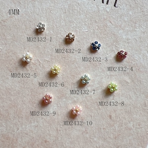 Pode incluir: Dez enfeites diferentes em forma de flor, cada um com uma cor e um design diferentes. Os enfeites estão dispostos em círculo sobre um fundo rosa claro. Os enfeites são etiquetados com o código do produto MD2432-1 a MD2432-10. Os enfeites têm 4 mm de tamanho.