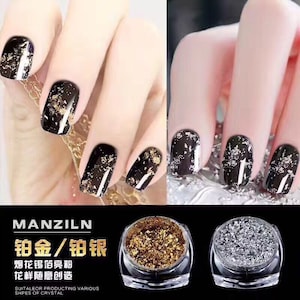 Puede incluir: Esmalte de uñas negro con escamas de pan de oro y plata. La imagen muestra uñas manicuradas con las escamas aplicadas. También se muestran dos pequeños frascos de escamas de pan de oro y plata. El texto "MANZILN" es visible.