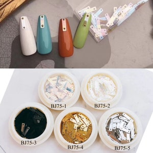 Puede incluir: Suministros para manicura con uñas pintadas y elementos decorativos. Las uñas están pintadas de blanco, verde azulado, naranja y verde, con detalles dorados. Pequeños recipientes contienen piezas de manicura en varios colores y acabados, etiquetados BJ75-1 a BJ75-5.