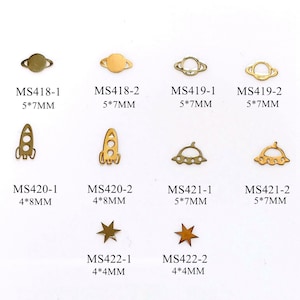 May include: Assortment of gold metal charms in various shapes, including planets, rockets, UFOs, and stars. The charms are arranged in rows on a white background. The charms are labeled with their size and product code.
