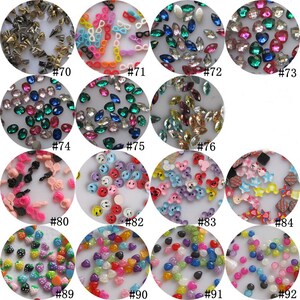 May include: Assortment of colorful plastic and rhinestone embellishments for crafts and nail art.  The embellishments include hearts, stars, smiley faces, and more.  The embellishments are arranged in circles with numbers next to them.