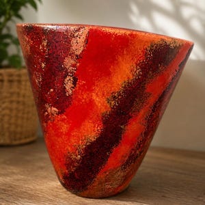 Könnte beinhalten: Eine konische Vase mit einer lebendigen, strukturierten Oberfläche, die wirbelnde Muster in leuchtendem Rot, tiefem Burgunderrot und metallischen Kupfertönen aufweist. Die Oberfläche zeigt ein gesprenkeltes, mehrschichtiges Aussehen.