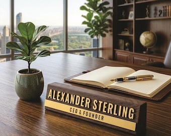 Op de afbeelding: Een houten naambordje met de tekst "ALEXANDER STERLING CEO & FOUNDER" in gouden letters. Een kleine potplant en een open notitieboek met een pen staan ook op het bureau. Het bureau is van donker hout.