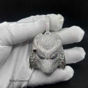 May include: A silver-toned pendant shaped like a creature head, fully encrusted with clear pavé stones. It features black stones for the eyes, a single red stone on the side, and a rectangular bail at the top. The text RubyDiamond is visible.