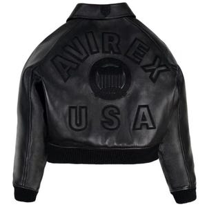 Op de afbeelding: Zwarte leren jas met de tekst "AVIREX USA" op de rug. De jas heeft een geribbelde zoom en manchetten, een kraag en een logopatch. De jas is een klassieke bomberstijl.