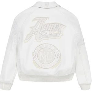 May include: A white leather bomber jacket featuring a classic collar, ribbed cuffs, and a ribbed hem. The back displays large embroidered patches with the text Avirex New York and a circular logo with the letters NYC and the words Trade Mark.