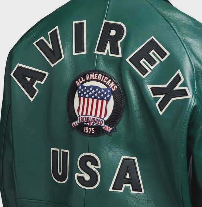 May include: Green leather jacket with white and black lettering spelling out "AVIREX" and "USA". A circular patch features a shield with the American flag and the text "ALL AMERICANS ESTABLISHED 1975 N.Y."