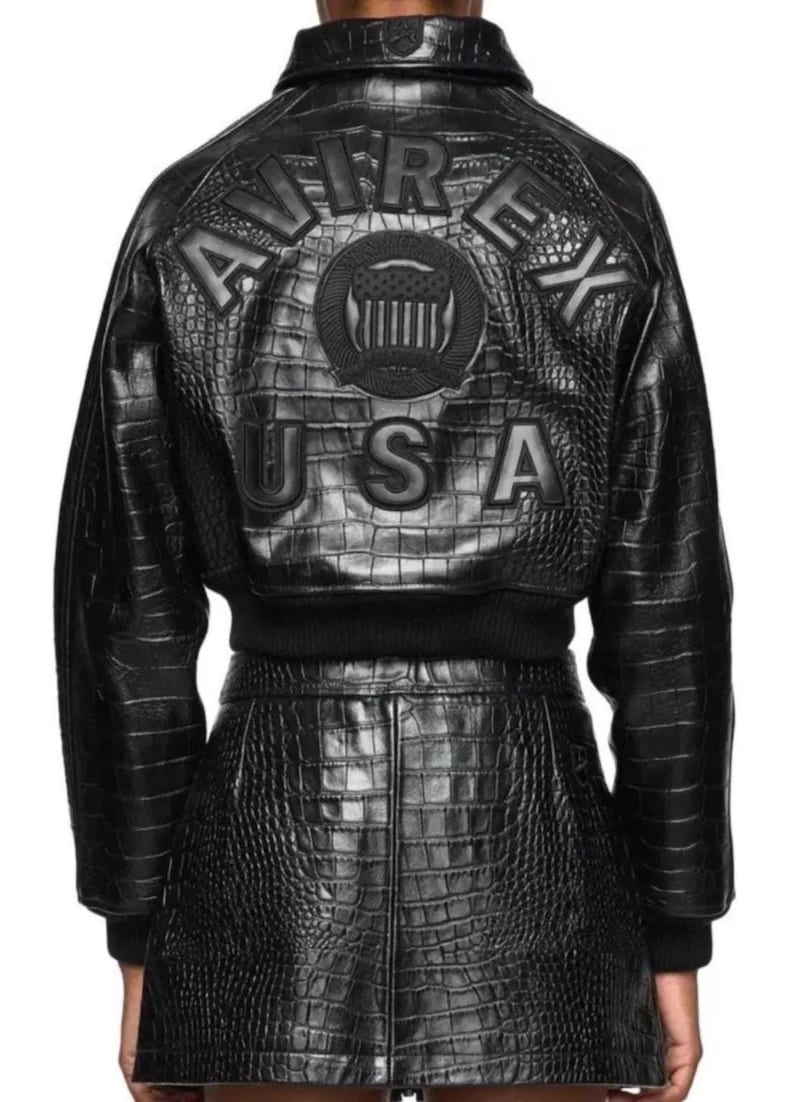 May include: A black jacket and matching skirt set featuring a crocodile-embossed texture. The back of the jacket displays the text AVIREX USA in large letters with a central circular emblem featuring a shield and stars design in black.