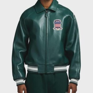 May include: A dark green leather jacket with a zip-up front and a collar. The jacket features a patch on the chest with the word "AVIREX" and a design with red, white, and blue colors. The cuffs and hem have white and black stripes.