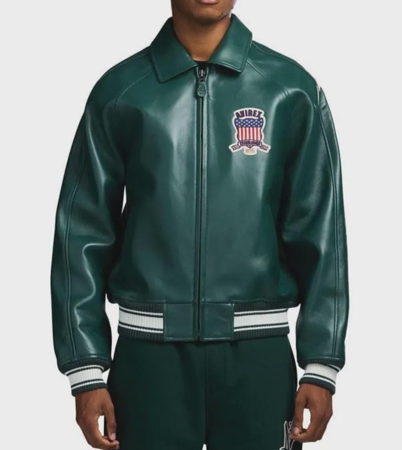 May include: A dark green leather jacket with a zip-up front and a collar. The jacket features a patch on the chest with the word "AVIREX" and a design with red, white, and blue colors. The cuffs and hem have white and black stripes.