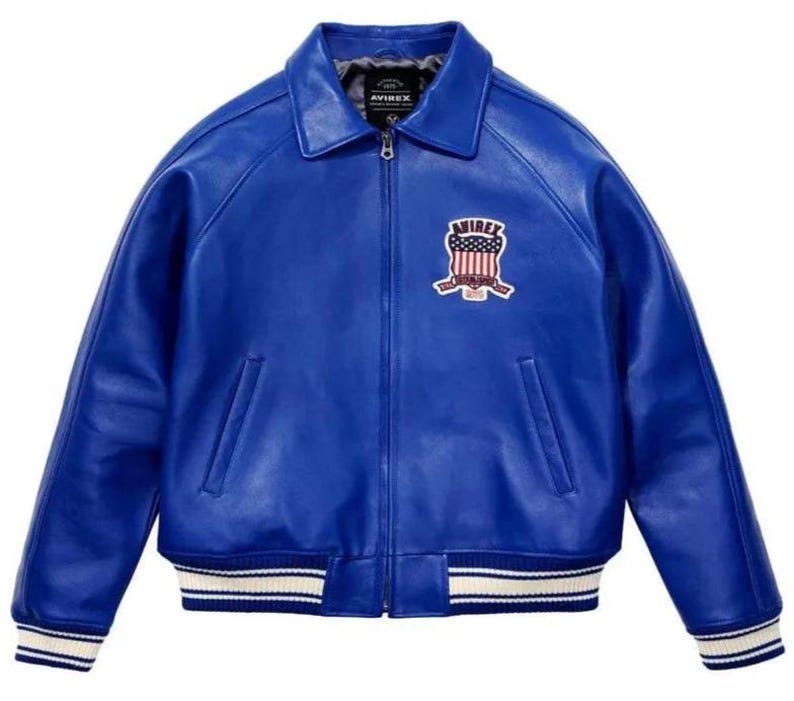 May include: A vibrant blue leather jacket featuring a full-length front zipper, a classic collar, and ribbed cuffs and hem with white and blue stripes. An embroidered patch on the left chest displays the text AVIREX with a flag-inspired shield design.
