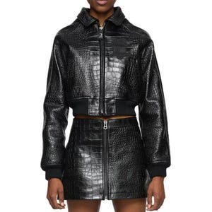 May include: A black cropped jacket and matching mini skirt set featuring a glossy crocodile-embossed texture. The jacket has a collared neckline, a full-length front zipper, and ribbed cuffs. The skirt features a central vertical zipper closure.
