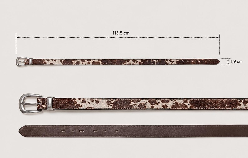 May include: A brown and white cow print belt with a silver-toned metal buckle. The belt measures 113.5 cm in total length and 1.9 cm in width. The underside of the belt is a solid dark brown leather material with visible adjustment holes.