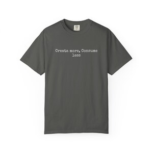 May include: Dark gray t-shirt with the text "Create more, Consume less" in a simple, sans-serif font. The shirt has a classic crew neck and short sleeves. The fabric appears to be a soft, comfortable material.