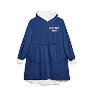 Pode incluir: Uma camisola com capuz azul-marinho de corte largo com forro e punhos brancos. A parte frontal apresenta o texto branco your text here acima de um bolso canguru central grande. A peça possui mangas compridas e um capuz integrado.