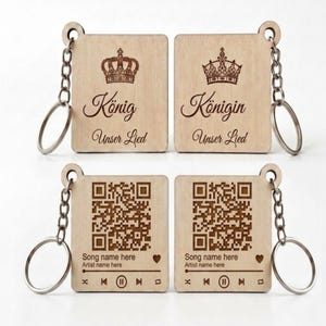 Könnte beinhalten: Vier rechteckige Schlüsselanhänger aus hellem Holz mit Metallringen. Zwei zeigen ein Kronensymbol, den Text König oder Königin sowie Unser Lied. Die anderen zwei zeigen einen QR-Code, den Text song name here, artist name here und Musiksymbole.