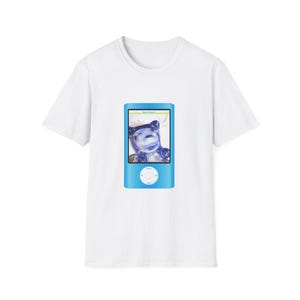 Pode incluir: Camiseta branca com um dispositivo azul semelhante a um iPod impresso. O dispositivo mostra uma imagem de um ursinho de goma azul. O dispositivo tem um painel de controle circular e uma tela pequena. O ursinho de goma está sorrindo.