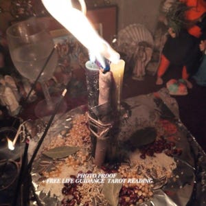 May include: Three tall candles in dark gray, light brown, and cream are bound together with twine and lit. They sit on a foil-covered surface scattered with dried beans, seeds, and bay leaves. Text reads: PHOTO PROOF + FREE LIFE GUIDANCE TAROT READING.