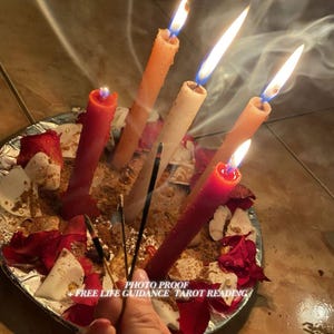 May include: A circular tray covered in red rose petals, brown powder, and white fragments, featuring four lit taper candles in red, orange, and cream colours. Three thin incense sticks are held in the foreground. Text reads: PHOTO PROOF FREE LIFE GUIDANCE TAROT READING.