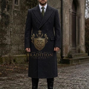 Puede incluir: Un abrigo cruzado de lana gris carbón con camisa blanca de cuello, corbata verde oliva y botas de cuero negro. Un escudo dorado con el texto THE TRADITION CRAFTER está centrado en la parte delantera del abrigo.