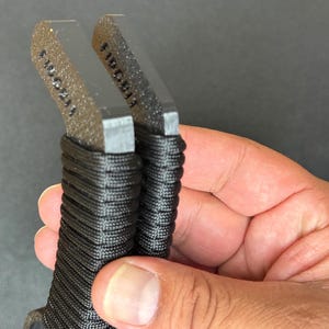 May include: Two metal tools with textured, dark grey, rectangular heads featuring the stamped text "LIDG813" on the top edges. The handles are wrapped in tight, black cordage, providing a secure grip for these functional, industrial-style implements.