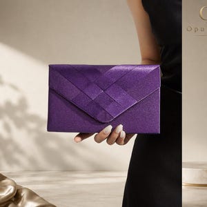 Op de afbeelding: Een rechthoekige paarse clutch met een geweven satijnen afwerking op de voorflap. Het accessoire in envelopstijl heeft een gestructureerd ontwerp met een puntige sluiting. De merknaam OpulAura is zichtbaar in de rechterbovenhoek van de afbeelding.