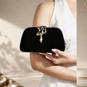Può includere: Una pochette in velluto nero con una chiusura in metallo dorato a forma di serpente centrata sul bordo superiore. La borsa rettangolare presenta angoli arrotondati e una texture scura e liscia, accentuata dalla decorazione metallica a serpente.