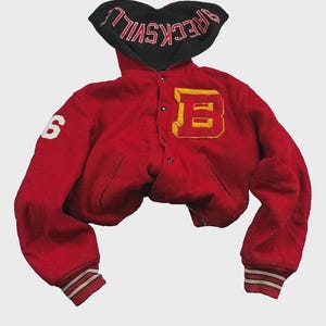 以下が含まれることがあります： ピンクでBRECKSVILLEの文字が刺繍された黒いフード付きの赤いバーシティジャケット。胸元には黄色と赤のBのワッペン、右袖には白い数字の6、袖口には赤と白のストライプが入ったリブ編みが施されています。
