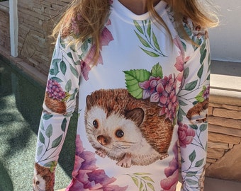 May include: White long-sleeved shirt with a watercolor print of hedgehogs, flowers, and leaves. The shirt has a crew neck and long sleeves.