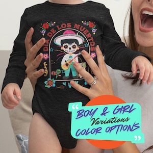 May include: A dark gray long-sleeve baby bodysuit featuring a colorful Dia de los Muertos design. The graphic includes a skeleton character playing a guitar, surrounded by flowers and the text "Dia de los Muertos".
