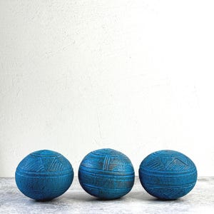 May include: Three spherical objects in a vibrant blue hue, each featuring a textured surface with intricate geometric patterns consisting of horizontal bands and triangular etchings. The spheres are arranged in a horizontal row, displaying a consistent matte finish and dark detailing within the carved grooves.
