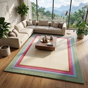 May include: A rectangular area rug featuring a large cream-colored center bordered by concentric rectangular frames in shades of orange, pink, light blue, and sage green, laid flat on a wooden floor in a room with a sectional sofa and coffee table.