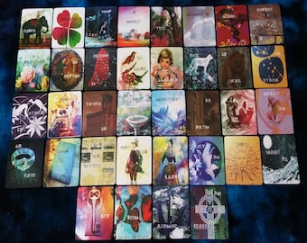 May include: A set of 36 tarot cards with colorful illustrations and text. The cards are arranged in rows and columns on a blue surface. The cards feature a variety of images, including animals, plants, and people.