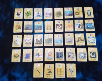 Puede incluir: Un juego de 36 cartas de tarot con ilustraciones de varios símbolos e imágenes. Las cartas están dispuestas en filas y columnas sobre una superficie azul. Las cartas están numeradas del 1 al 36.